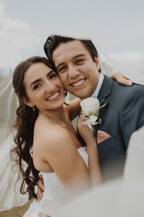 A bride and groom are posing together with a bouquet of white flowers.